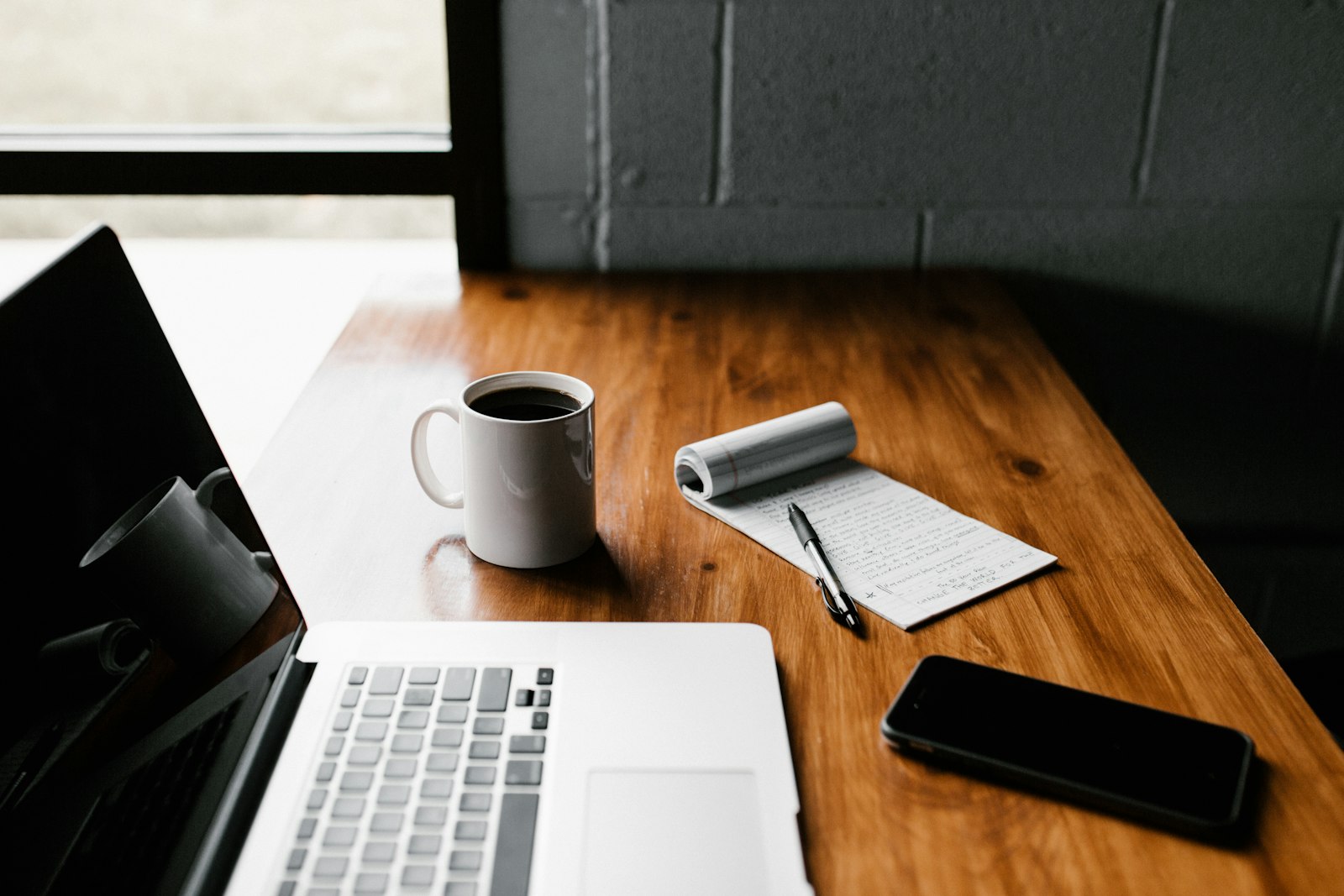 A tidy desk workspace with a laptop, coffee and a notepad of search-planning notes
