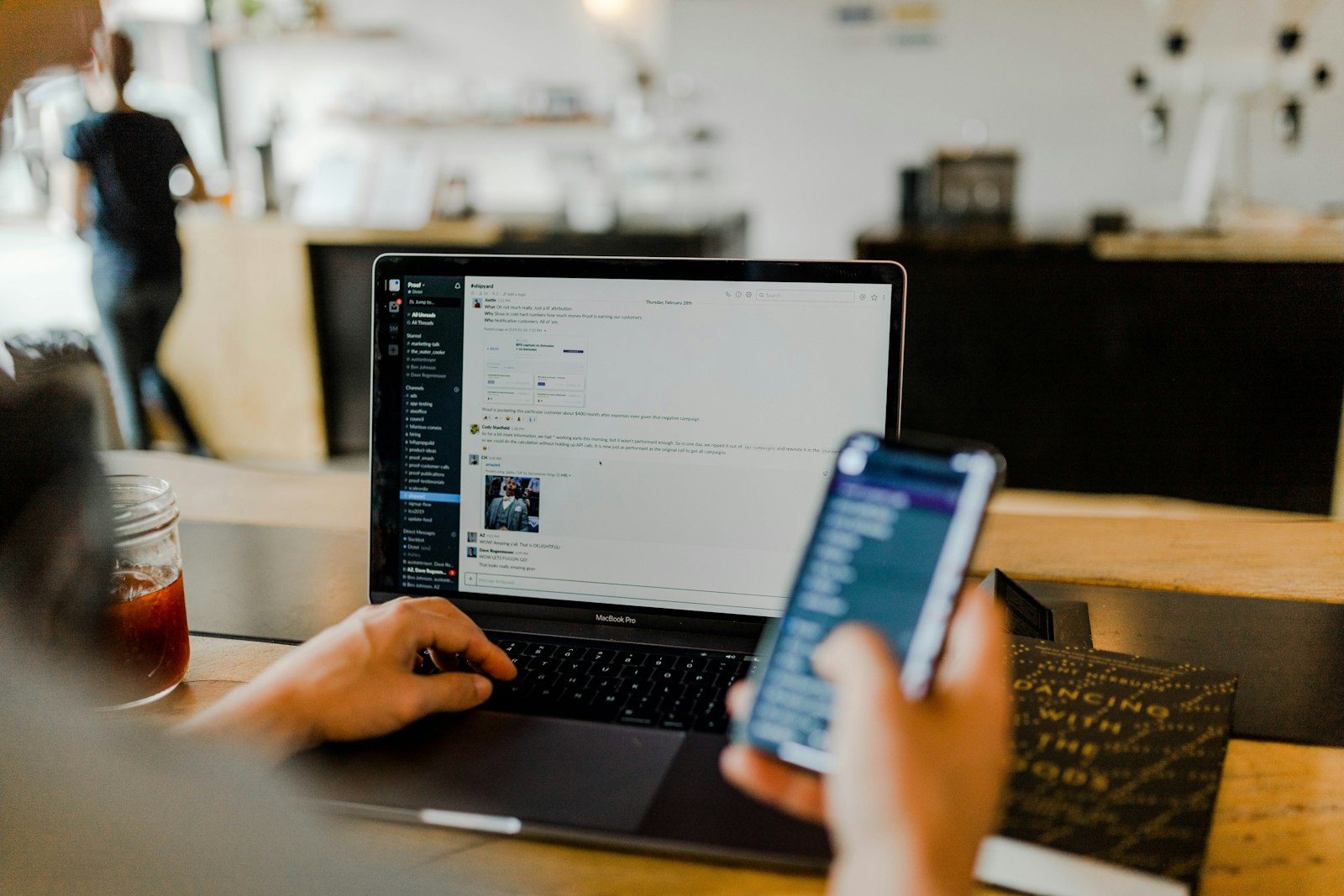 A person managing social feeds across a laptop and phone in a café